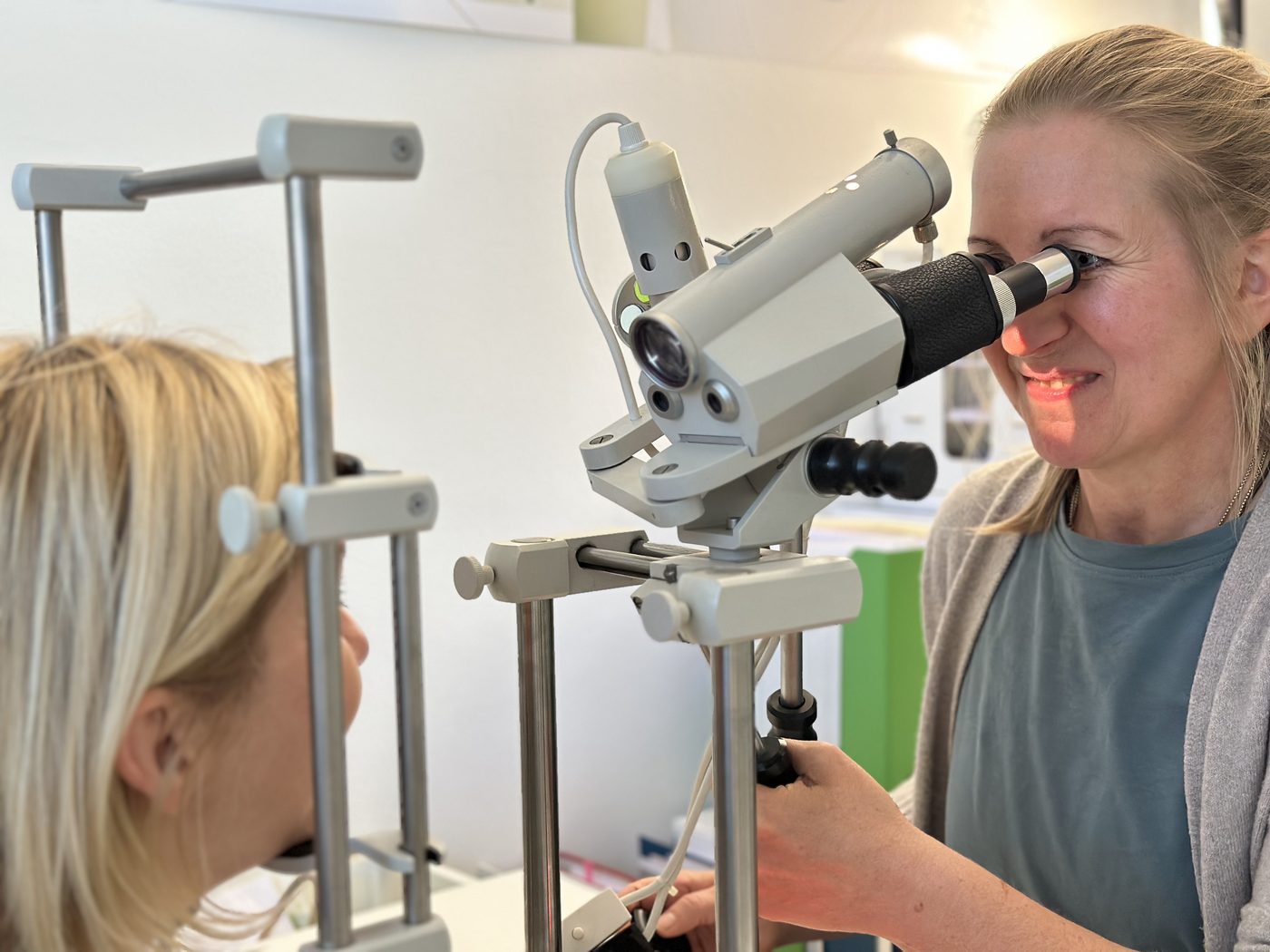 Delia Gröninger blickt durch das Irismikroskop, die Patientin hat ihr Kinn auf die Stütze gelegt.