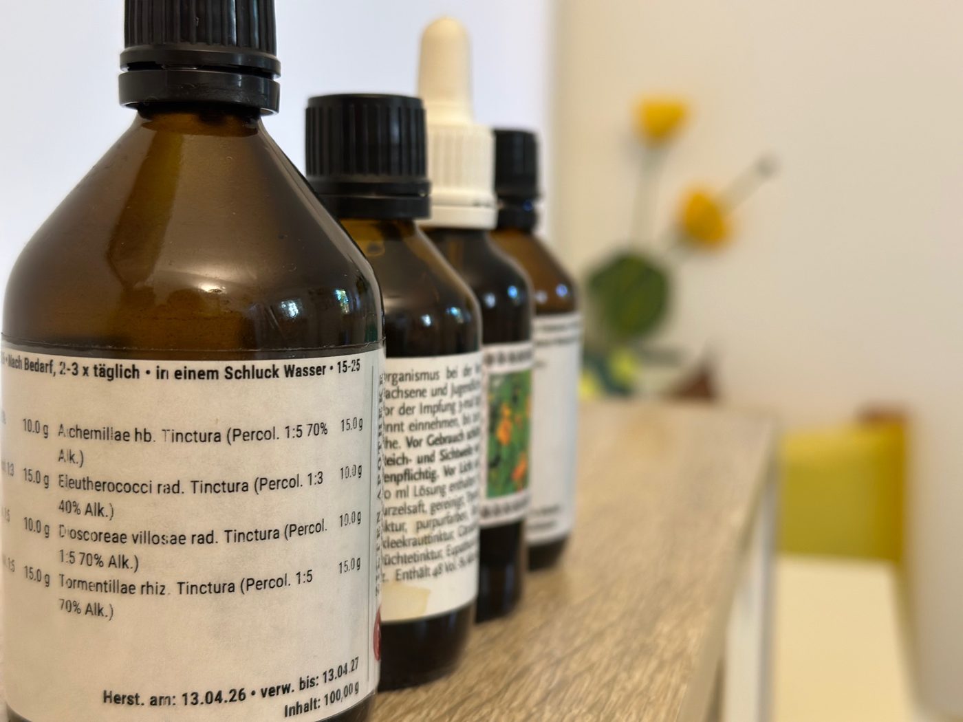Braune Apothekenflaschen mit Tinkturen in einer Reihe, auf dem vorderen Etikett eine Rezeptur aus Frauenmantel, Taigawurzel, Yamswurzel und Blutwurz.