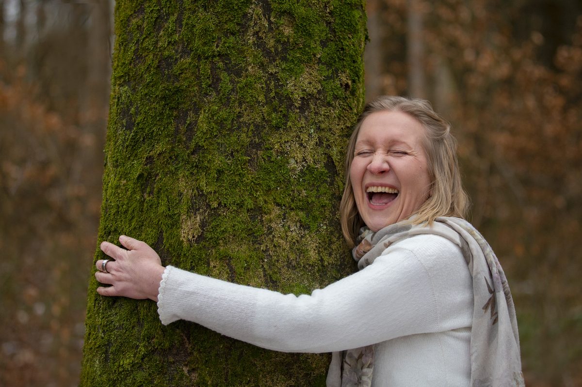 Delia Gröninger lachend, einen Baum umarmend